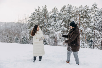 Fototapeta na wymiar Happy couple spending fun time outdoors, throwing snow, on a cold winter day.