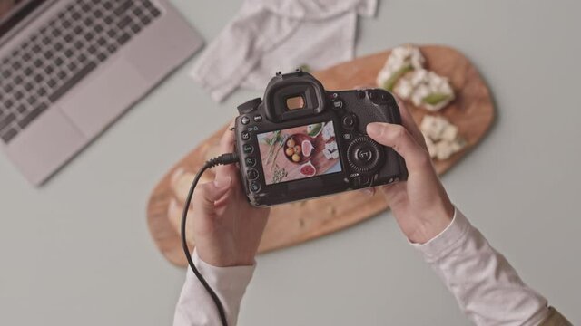 Top view shot of unrecognizable female food photographer with camera taking pictures of beautifully arranged blue cheese bruschetta with tomatoes and figs on wooden plate