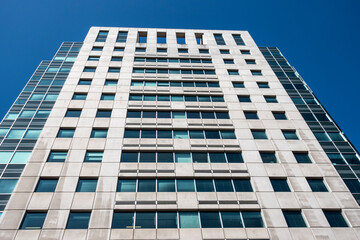 Angled view of a large, window covered apartment building corner against a blue, cloud filled sky