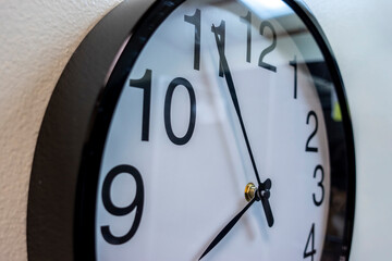 Close up focus on a large, black and white wall clock hung up on a beige colored wall