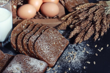 Fresh loaves of bread with wheat and gluten on a black table. Bakery and grocery concept. Fresh, healthy sorts of rye and white loaves food closeup. Fresh homemade bread with cereals.