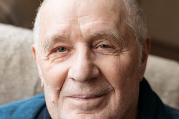 Close up portrait of old smiling man looking at camera. He is open-eyed and cheerful. Smiling blue eyes of a happy senior man 