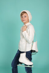 a blue-eyed boy in a white knitted sweater and a winter hat holds figure skating skates in his hands