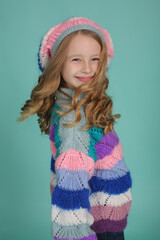 beautiful happy blonde girl in a colored knitted sweater and hat on a blue background