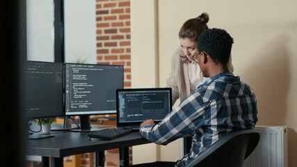 Two programmers doing high five hand gesture at desk with multiple screens running code celebrating...