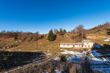 Old stone farmhouse with green and brown pastures in winter. Lessinia Plateau (Altopiano della...