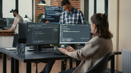 Focused software developer writing code looking at multiple computer screens displaying machine...