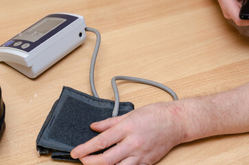 A mature man holds a digital blood pressure monitor on the table