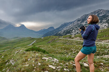 Fototapeta na wymiar Young woman with camera enjoying dramatic view of mountains of Durmitor, Montenegro on storm day.