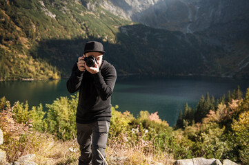Young  man photographer taking photographs with digital camera in a mountains.