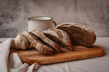 a loaf of bread on the table, sliced bread on a wooden cutting board with garlic and white  cup