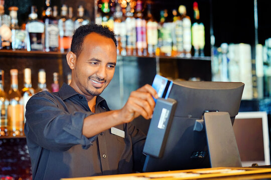 African man bartender in hotel bar. African male bartender at the cash register