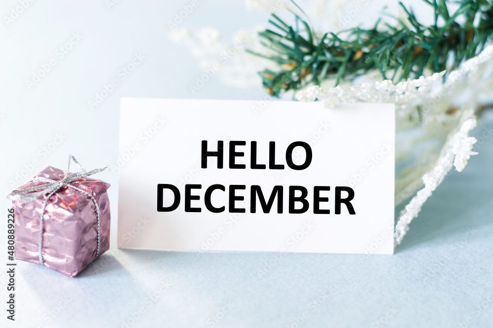 Poster hello december text on a white card on the table next to a gift in a package and spruce branches