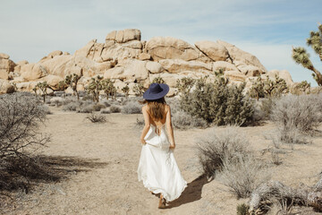 Woman in boho style dress and hat rushing through the Joshua Tree desert landscape