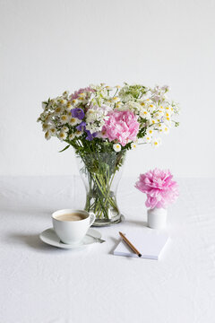 Studio shot of cup of coffee and bouquet of peonies, feverfews (Tanacetum parthenium), bellflowers (Campanula) and white laceflowers (Orlaya grandiflora)