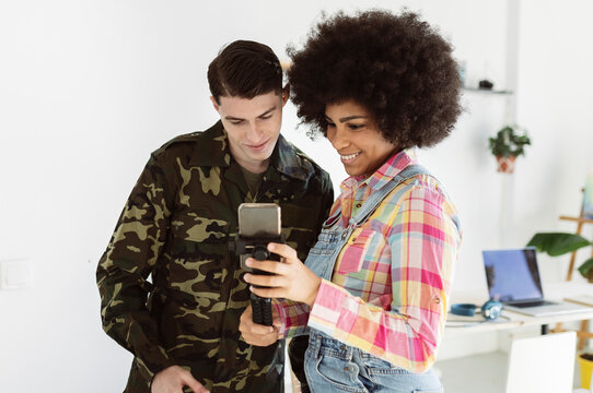 Smiling woman sharing smart phone with young soldier man at home