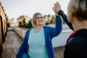 Happy overweight woman high fiving with personal trainer outdoors on gym terrace. - obrazy, fototapety, plakaty