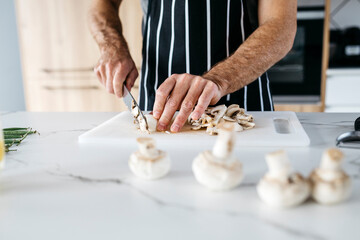 Man slicing mushroom in kitchen at home