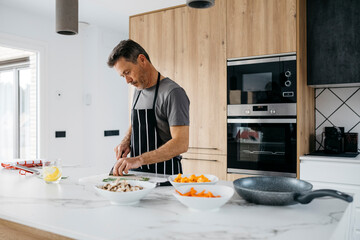 Man wearing apron cutting vegetables in kitchen at home
