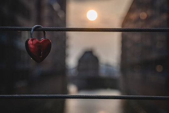 Love lock hanging on bridge railing with setting sun in background