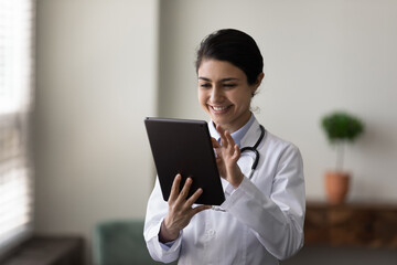 Happy young Indian female doctor physician therapist using software apps on digital touchpad...