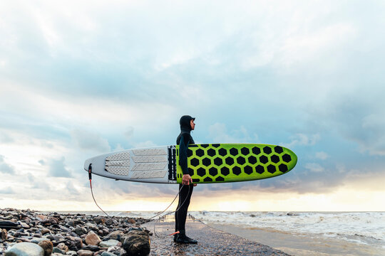 Surfer holding surfboard standing on pier at sunset