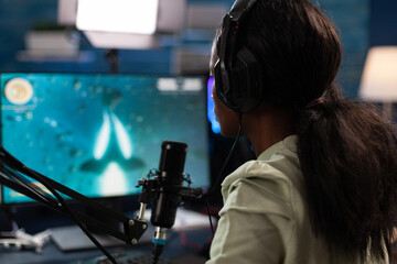 Successful esport gamer wearing headset talking with remote players during live streaming using gaming microphones. Concentrated player playing space shooter videogames during online championship