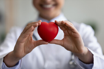 Close up focus on heart figure in hands of female Indian cardiologist physician doctor, advertising regular annual healthcare checkup or medical services, preventing diseases, donation charity concept