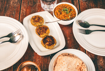 Simple Indian vegetarian home food served at a table. Soya keema and Aloo tikki served with Roti bread on a white plate on a wooden table.