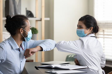 Happy young African American male patient touching elbows with Indian female general practitioner...