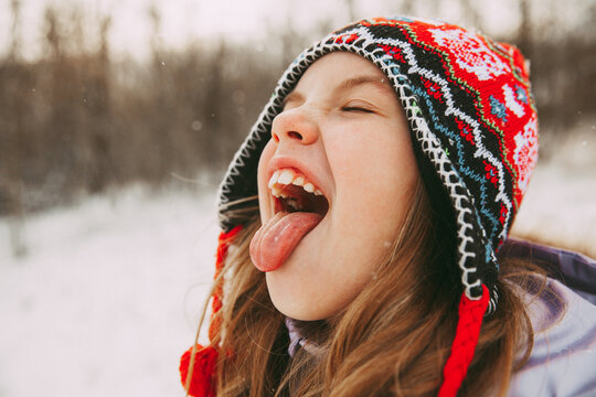 smiling little girl in a knitted hat catches snowflakes with her tongue.