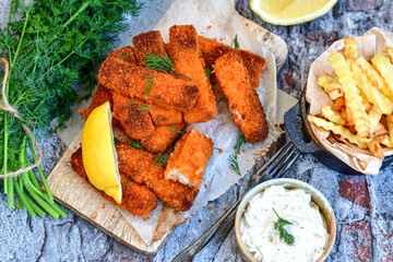 Close up of   Crispy breaded  deep fried fish fingers with breadcrumbs served  with remoulade sauce and  lemon Cod Fish Nuggets on rustic wood table background