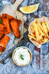 Close up of   Crispy breaded  deep fried fish fingers with breadcrumbs served  with remoulade sauce and  lemon Cod Fish Nuggets on rustic wood table background