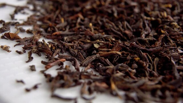 Black dried tea leaf. Macro. Rotation. On white surface