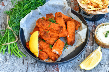 Close up of   Crispy breaded  deep fried fish fingers with breadcrumbs served  with remoulade sauce and  lemon Cod Fish Nuggets on rustic wood table background