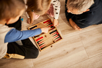 Children playing backgammon with grandfather at home