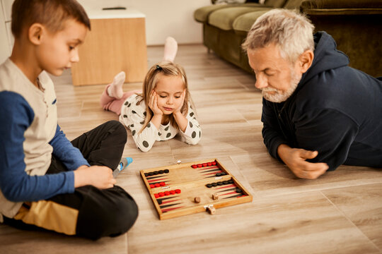 Boy and girl playing backgammon with grandfather at home