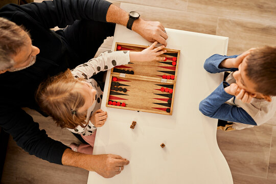 Grandfather playing backgammon on table with grandchildren at home