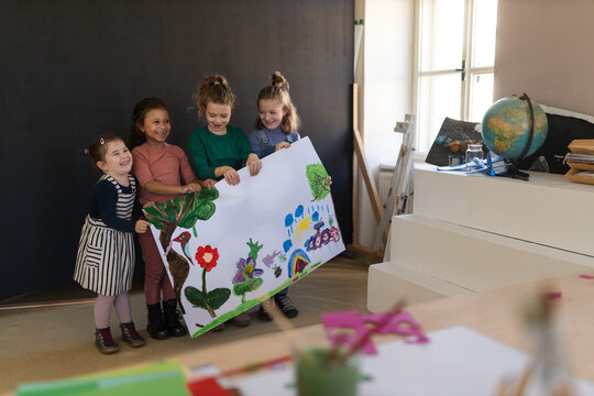 Group of little girls holding a picture they painted during creative art and craft class at school