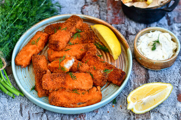Close up of   Crispy breaded  deep fried fish fingers with breadcrumbs served  with remoulade sauce and  lemon Cod Fish Nuggets on rustic wood table background