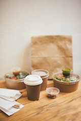Takeaway food in containers and disposable bowls on wooden table on white background. Food delivery and takeout. Place for text.