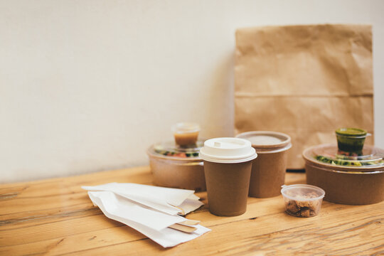 Takeaway food in containers and disposable bowls on wooden table on white background. Food delivery and takeout. Place for text.