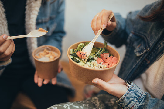 Two Young Women Female Friends Sitting Outdoors Eating Takeaway Food, Laughing And Having Fun. Food Delivery And Takeout.