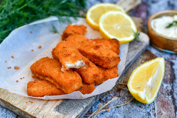 Close up of   Crispy breaded  deep fried fish fingers with breadcrumbs served  with remoulade sauce and  lemon Cod Fish Nuggets on rustic wood table background