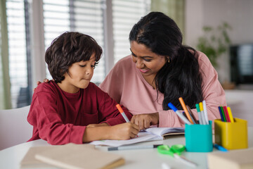 Little multiracial boy doing homework with his mother at home.