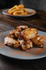 Spicy fried chicken wings in a plate on a wooden table sprinkled with spices. Vertical orientation, copy space, no people, close-up, dark moody