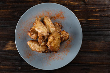 Spicy fried chicken wings in a plate on a wooden table sprinkled with spices. Horizontal orientation, copy space, no people, top view