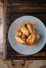 Spicy fried chicken wings in a plate on a wooden table sprinkled with spices. Vertical orientation, copy space, no people, top view