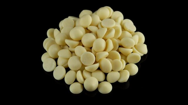 White chocolate chips on black background, rotation. Chocolate chips. Confectionery concept. 4K UHD video