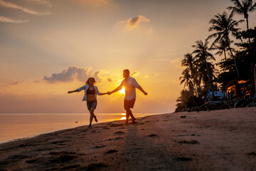 Young happy couple dancing on tropical beach at sunset, honeymoon travel concept